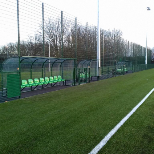 Two green 10 seater dugouts installed at a football pitch with smaller managers 4 seat bespoke shelter installed in the middle.